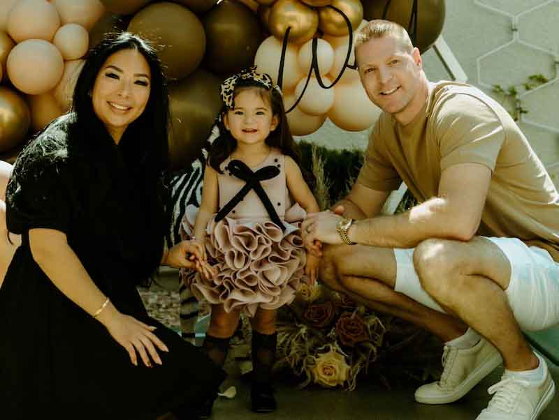 two adults and a child standing in front of balloons 