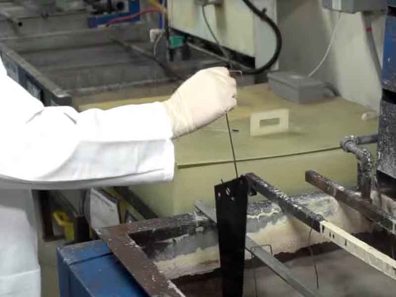 person dipping part in black oxide tank