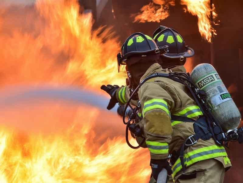 two firefighters with hose battling a fire